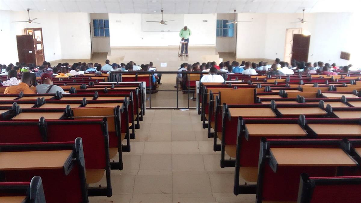 Vaste amphithéâtre universitaire vu depuis les rangs du fond, un enseignant donne cours à l'estrade