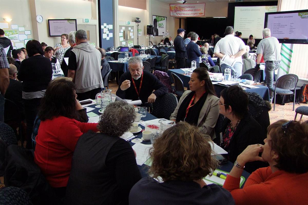 Atelier d'éducation des adultes : des participantes et participants discutent par tables de travail, documents en main