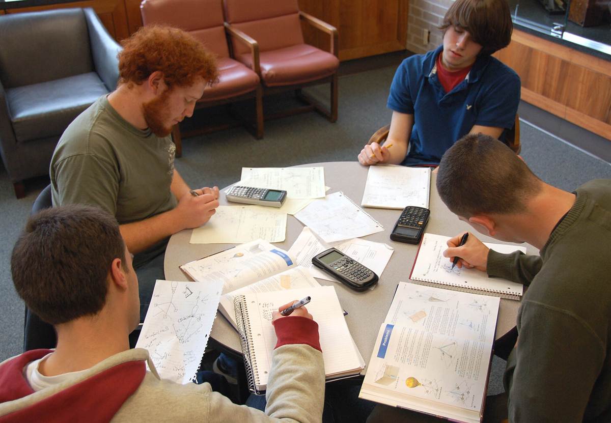 Quatre étudiants travaillent ensemble autour d'une table ronde couverte de cahiers, de manuels et de calculatrices